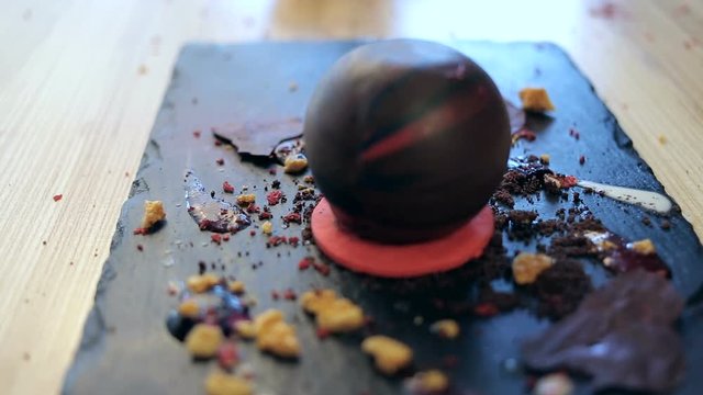 dolly shot of put on a chocolate sphere on a plate for decoration dessert. Dessert decorated with a cream, honey crumbs and picies of chocolate. Making in a restaurant.