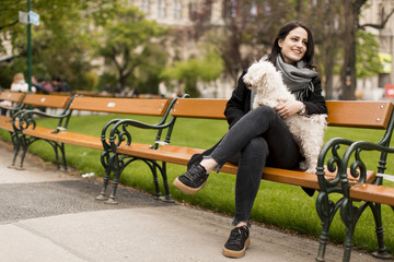 Young woman sitting in the park and holding a small dog in her lap