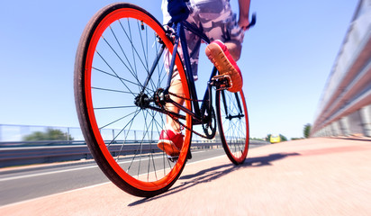 Fototapeta na wymiar Man cycling on sport bike - Bicycle wheels and road perspective with cyclist riding blue summer sky background - Concept of alternative transportation environmental friendly 