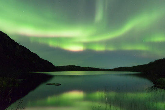 The Aurora in the sky above the hills . Reflected in the lake.