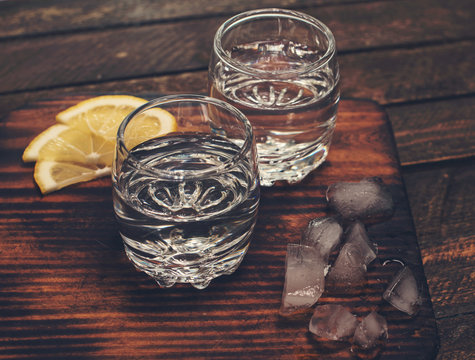 Gin tonic, vodka or rum with ice and lemon on wooden table. Retro styled background.