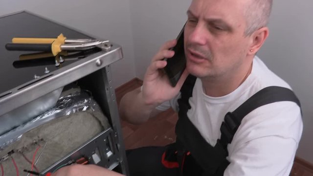 Electrician with screwdriver and smart phone near electric cooker
