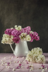 still life with purple and white lilac in white vase on pink table, spring blooming plant with petals