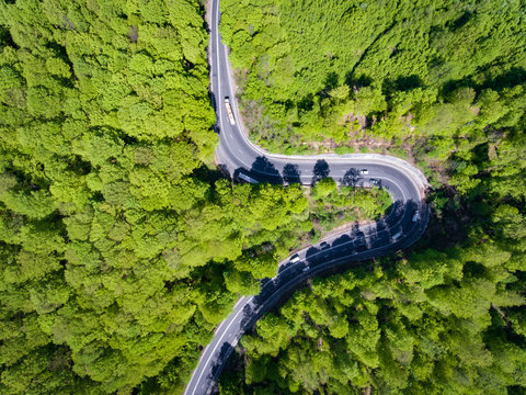 Forest curved road with trucks and cars on it. Aerial view from a drone.
