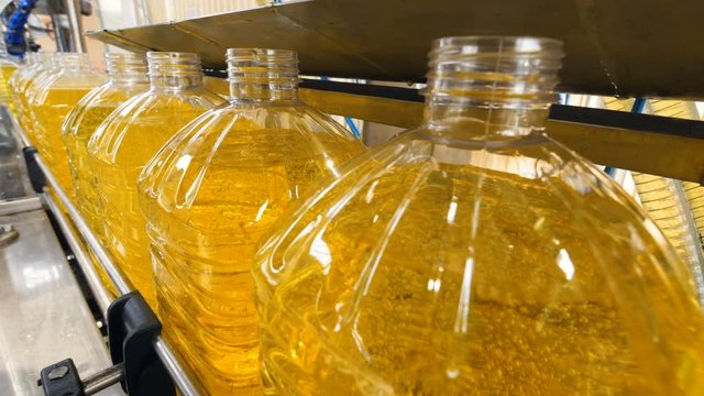 Close-up. Industrial conveyor with plastic bottles filled with yellow liquid. 4K.
