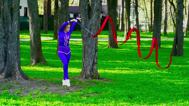 Young gymnast dacing with the ribbon in the park slow motion