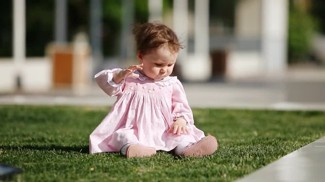 Happy baby-girl seated on the green grass in the park and playing.