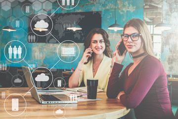 Two young businesswomen sitting in cafe at table and talking on cell phones.