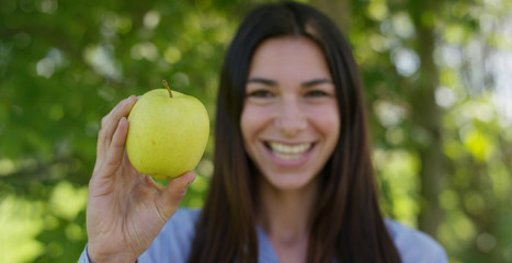 Beautiful young girl holding a fresh ripe green apple in the hands, in the background of nature. Concepts: biology, bio products, bio ecology, growing fruit, diet, natural clean and fresh product.