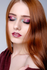 Pretty young redghead woman's studio portrait on gray background, pink makeup