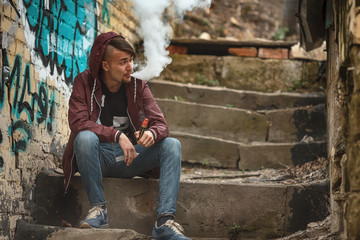 Vape man. Photo of a handsome young white guy in the hood vaping and letting off steam from an...