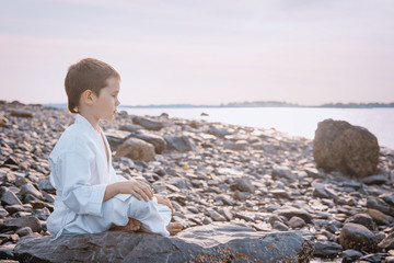 Boy in a kimono meditating on the beach. kid in lotus position