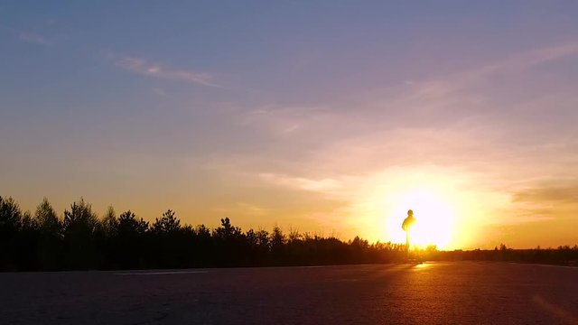 Silhouette of a guy driving a segway into sunrays at sunset. Slow Mo.