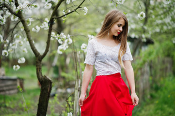 Portrait of beautiful girl with red lips at spring blossom garden, wear on red dress and white blouse.