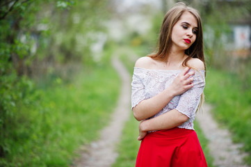 Portrait of beautiful girl with red lips at spring blossom garden, wear on red dress and white blouse.