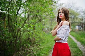 Naklejka na ściany i meble Portrait of beautiful girl with red lips at spring blossom garden, wear on red dress and white blouse.