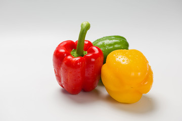 Three bulgarian peppers of different colors lie in a row on a white background.