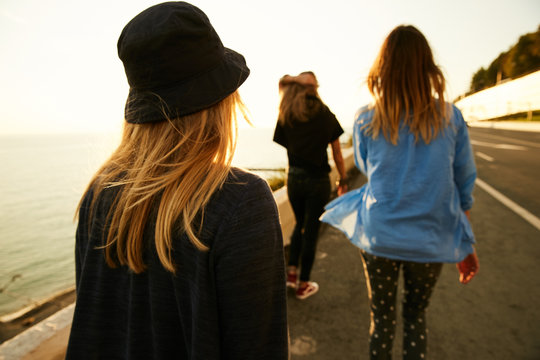 Girls travelers walking down the roadside on the sea coast on the sunset