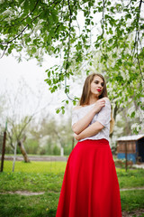 Naklejka na ściany i meble Portrait of beautiful girl with red lips at spring blossom garden, wear on red dress and white blouse.