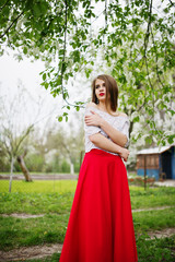 Portrait of beautiful girl with red lips at spring blossom garden, wear on red dress and white blouse.