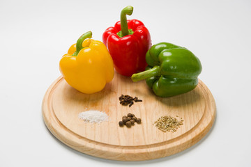 Three bulgarian peppers of different colors lie in a row on a wooden cutting board. Peppers with various spices. White background. 