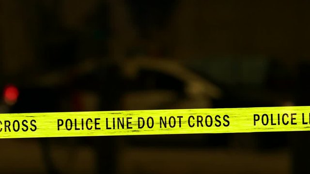 Crime scene tape with defocused flashing police car siren in background