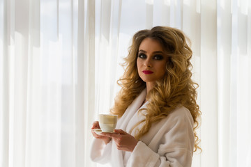 Beauty girl drinking coffee. Beautiful woman opening curtains, looking out the window and enjoying her morning coffee