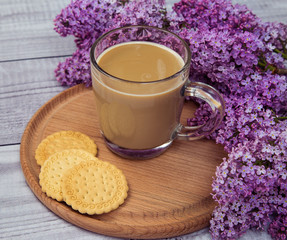 glass coffee Cup with cookies and milk on a background of purple lilac on a wooden stand