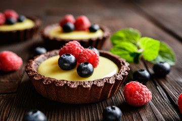 Cocoa tartlets filled with vanilla pudding and topped with blueberry and raspberry