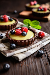 Cocoa tartlets filled with vanilla pudding and topped with blueberry and raspberry