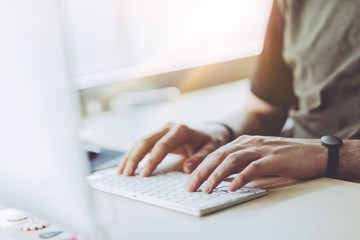 Young businessman working at sunny office on laptop, Man using desktop computer at home while sitting the wooden table