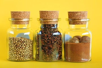 Nutmeg, white pepper and clove spice  in a glass bottle on a bright yellow background