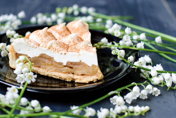 Apple pie with whipped cream. Pie of apples with meringue on a dark background. Apple pie and lily of the valley.