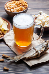 Lager beer mug and snacks on wooden table. Nuts, chips, crackers and dry fish