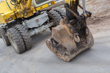 Fototapeta premium Work excavator at the construction site. The dirty excavator works on the construction site and repairs the road surface.