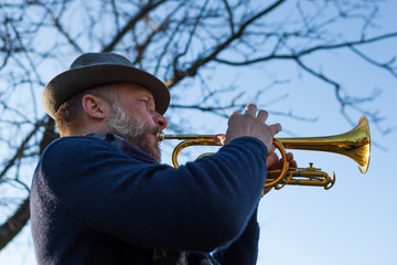 An elderly musician plays in the street on a trumpet in spring day