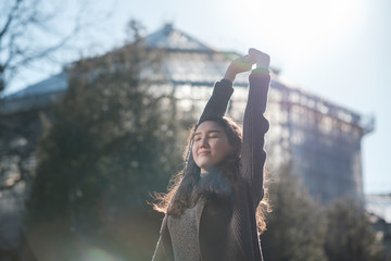 A beautiful Asian girl is standing in the park and resting, basking in the sun. Enjoy the silence in city life.