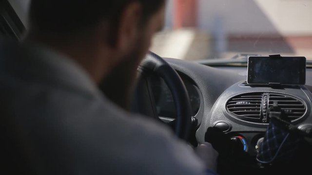 A man gets into the car and turns on the navigator on the smartphone
