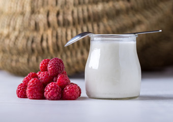 White yogurt with raspberries in glass bowl on white table.