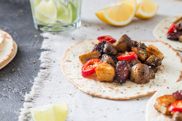 Tacos with grilled mushrooms, Spanish spicy sausage chorizo, Mexican tortillas, Cypriot cheese halloumi, hot chilly, dried oregano. With glass of water with lime and lemon on cloth background