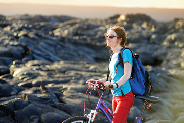 Young tourist cycling on lava field on Hawaii. Female hiker heading to lava viewing area at...