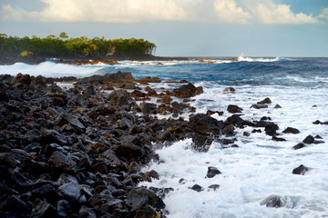 Beautiful pink tinted waves breaking on a rocky beach at sunrise on east coast of Big Island of Hawaii