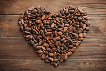Heart made of aromatic cocoa beans on wooden background