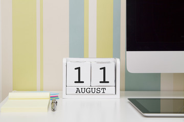 Cube shape calendar for AUGUST 11 and computer with white screen on table. 