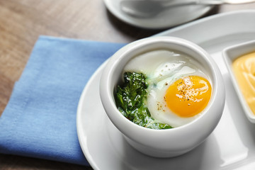 Plate with tasty egg and spinach on wooden table