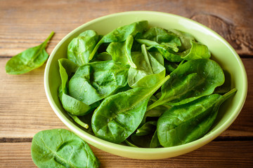 Washed fresh spinach leaves in bowl on rustic wooden table.