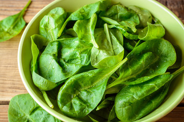 Washed fresh spinach leaves in bowl on rustic wooden table.