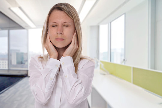 Business woman suffering from headache, covering her ears, because of noise in an office