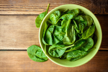 Washed fresh spinach leaves in bowl on rustic wooden table.