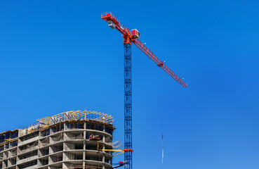 Construction site. Construction crane and high-rise building under construction against blue sky.